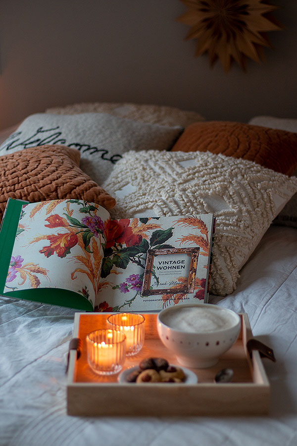 Gemütlichkeit im Schlafzimmer mit vielen Kissen, einem guten Buch und Kaffee oder Tee